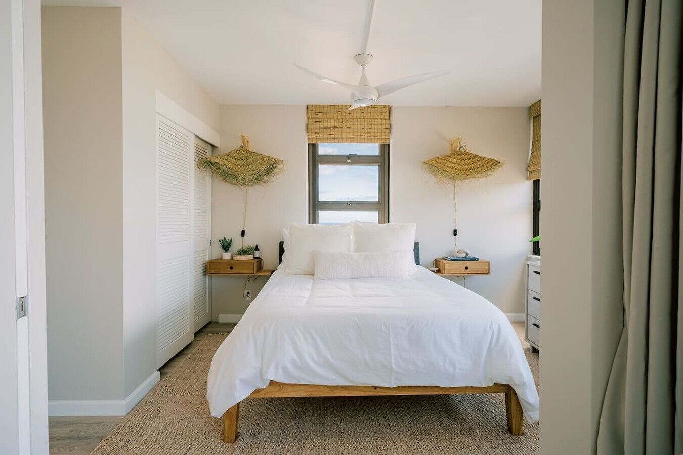A bedroom with a bed, bedside tables, a ceiling fan, and a window with a view.