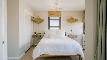 A bedroom with a bed, bedside tables, a ceiling fan, and a window with a view.