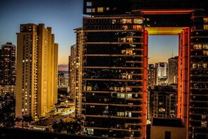 A high-rise building with multiple floors, a prominent red arch structure, and surrounding taller buildings. - Modern Waikiki Studio Oasis (Honolulu)