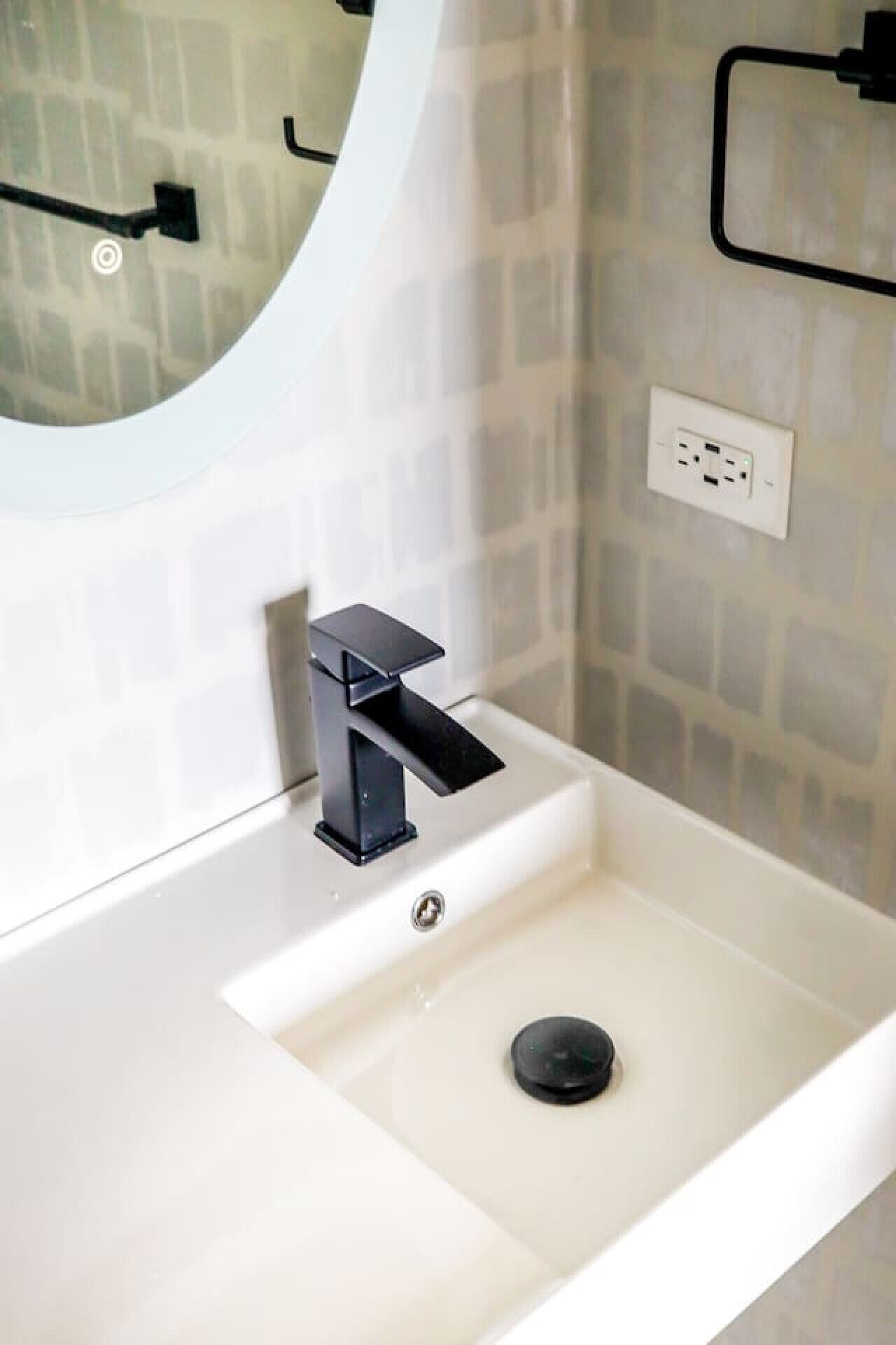 A bathroom with a white sink, black faucet, and a mirror with a circular frame.