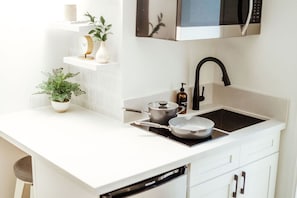 A modern kitchen with white cabinetry, a black faucet, a microwave, and a pot on the stove. - Modern Waikiki Studio Oasis (Honolulu)