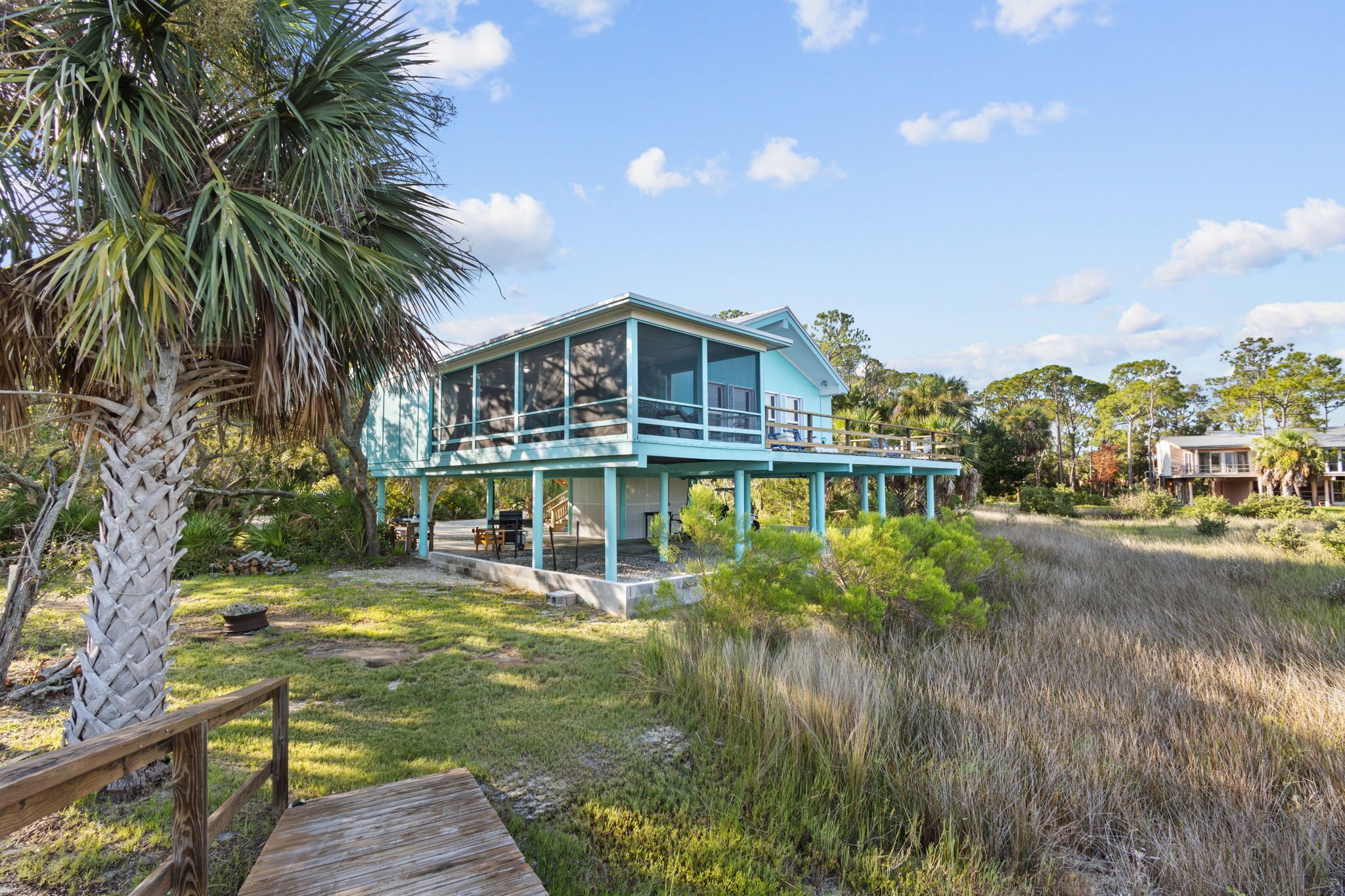 A two-story house with a balcony, surrounded by natural vegetation and a wooden deck.