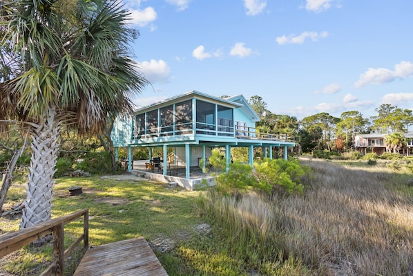 A two-story house with a balcony, surrounded by natural vegetation and a wooden deck.