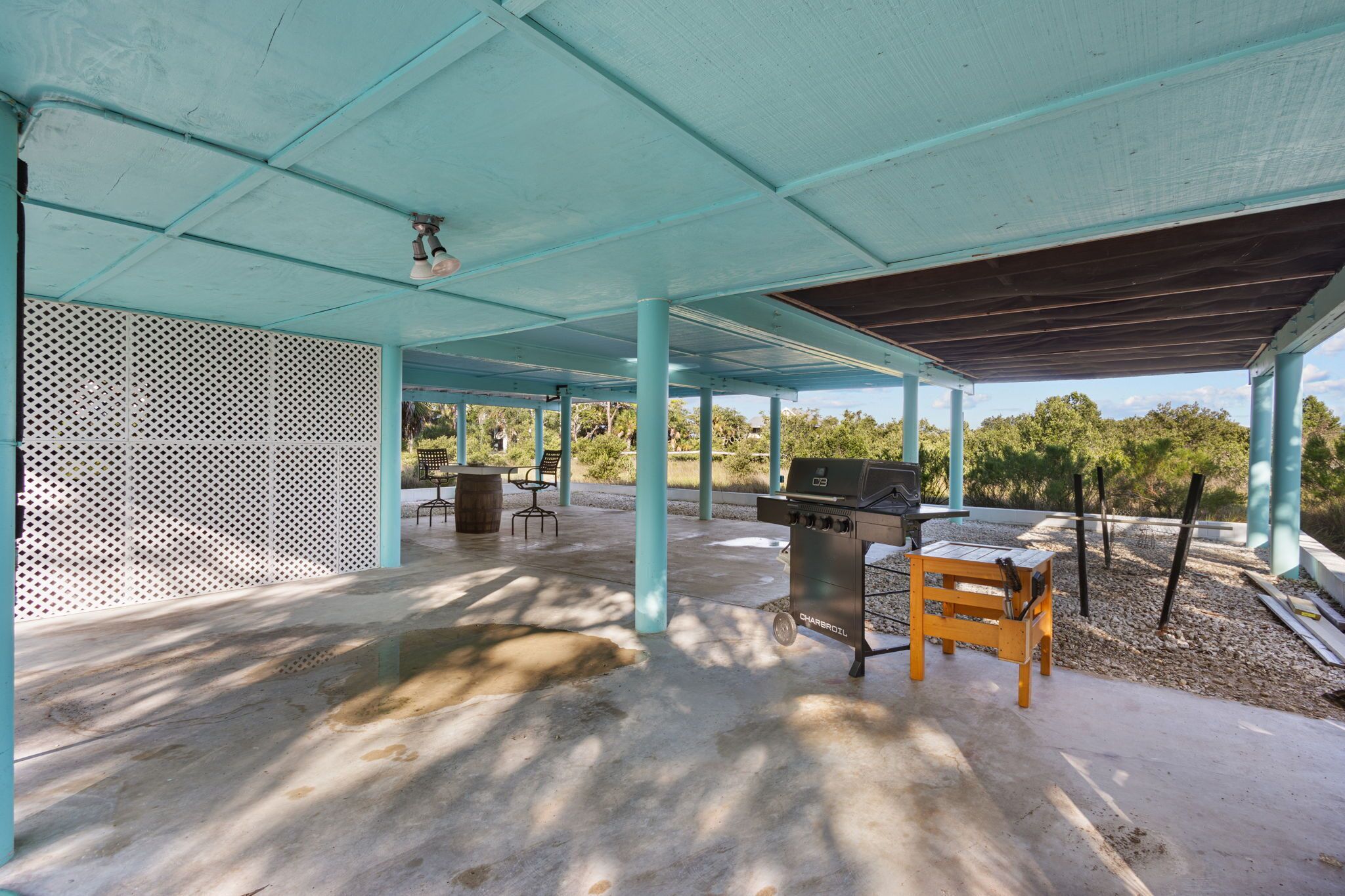An outdoor covered patio area with a barbecue grill, seating, and a view of the surrounding landscape.
