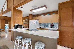 A modern kitchen with wooden cabinetry, a white countertop, and bar stools.