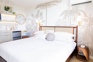 A hotel room with a bed, bedside tables, a desk, and a kitchenette. - Ocean Breeze Bungalow Across Waikiki Beach (Honolulu)