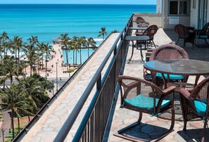 A balcony with wicker furniture overlooking a beach and ocean. - Ocean Breeze Bungalow Across Waikiki Beach (Honolulu)
