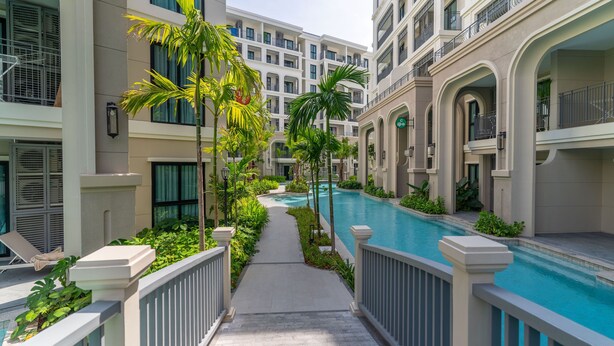 A modern hotel with a central swimming pool, surrounded by lush greenery and multiple balconies. - The Title Legendary 2BR, 5 Min to Bang Tao Beach (Tambon Choeng Thale)
