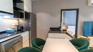 A modern kitchen with a microwave, refrigerator, and coffee maker. There is a dining area with a table and chairs. A bed and a TV are visible in the background. - The Title Legendary 2BR, 5 Min to Bang Tao Beach (Tambon Choeng Thale)
