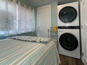 A bedroom with a bed, a washing machine, and a shelf with a bottle. - Two Waterfront Cottages in Cedar Key Amazing View! (Cedar Key)