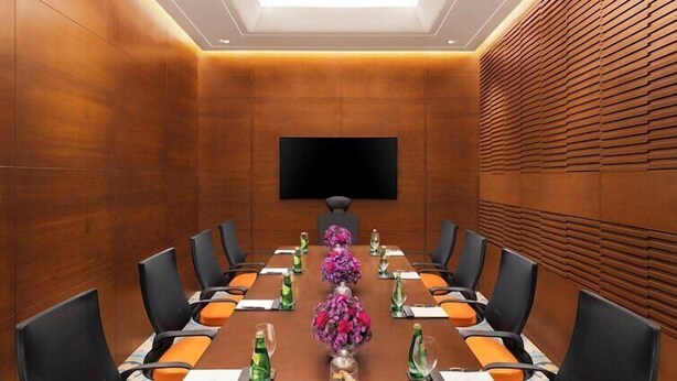Una sala conferenze con un lungo tavolo, sedie e uno schermo televisivo.