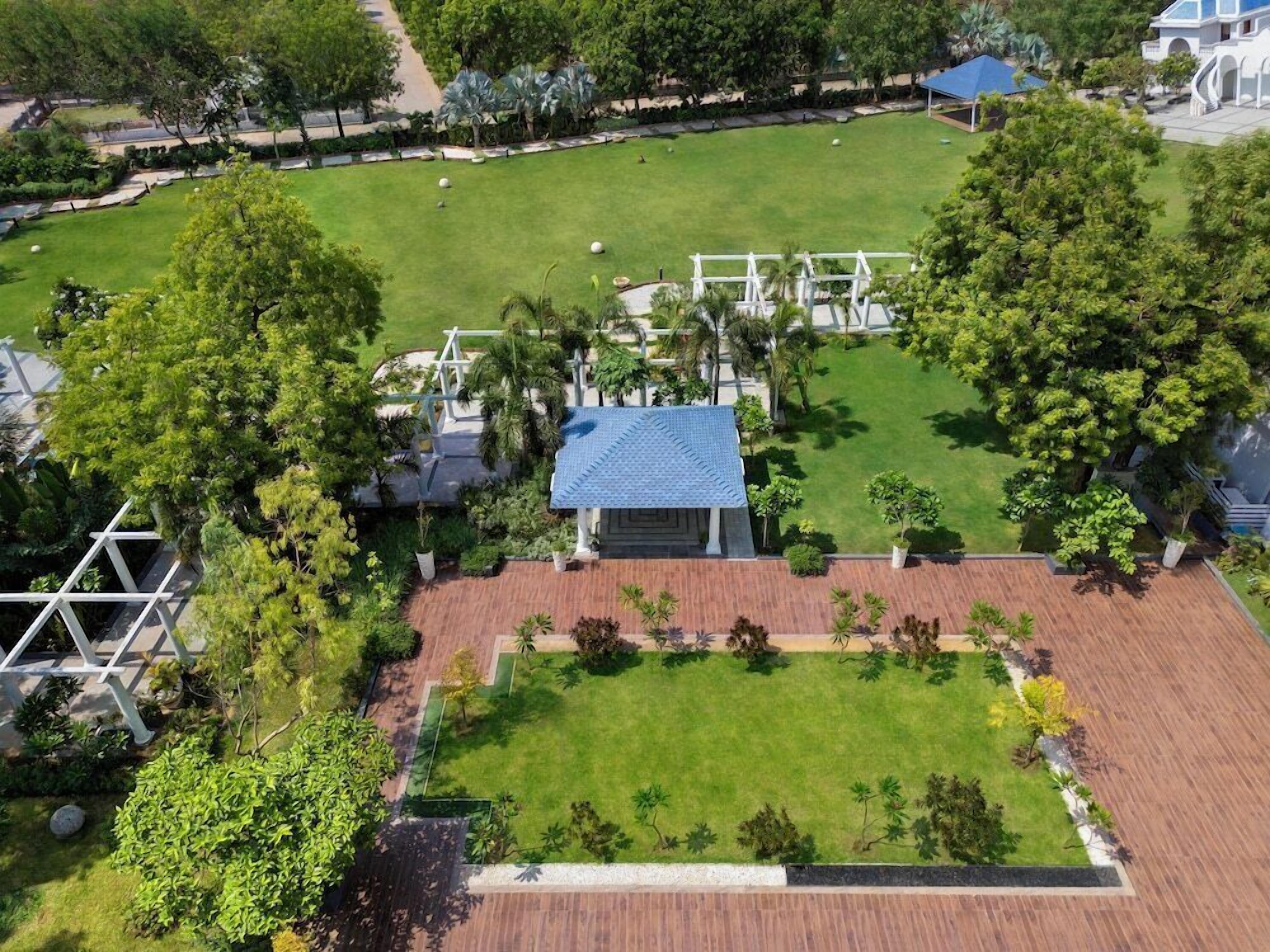 An aerial view of a landscaped property with a central lawn, a pavilion, and surrounding greenery.