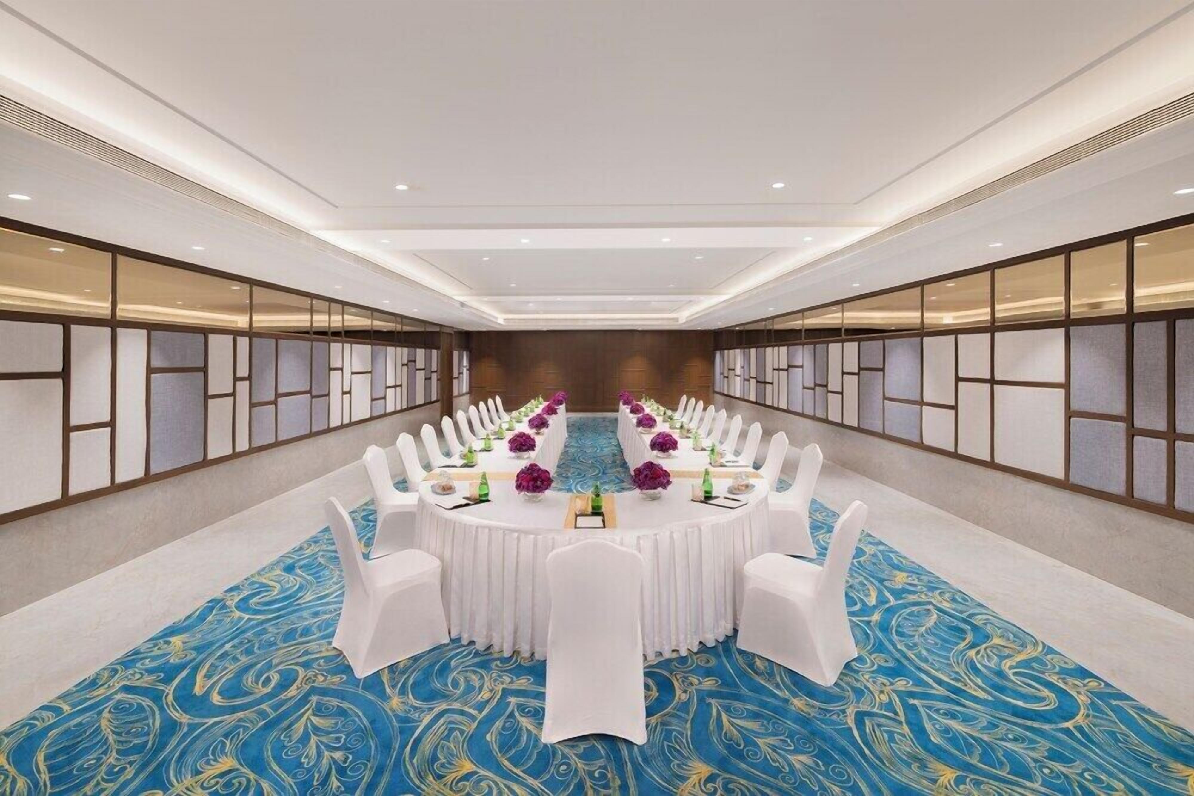 A conference room with a long table, white chairs, and a blue patterned carpet.