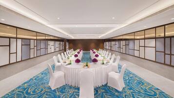 A conference room with a long table, white chairs, and a blue patterned carpet.