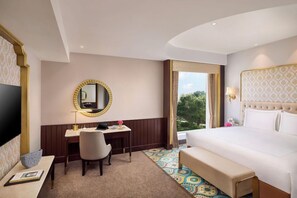 A hotel room with a bed, a desk, a chair, a television, and a large window with a view. - Taj Gandhinagar Resort and Spa (Mansa)
