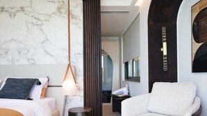 Ein modernes Hotelzimmer mit Marmorwand, einer hängenden Pendelleuchte, einem großen Fenster und einer Sitzecke mit weißem Sessel.