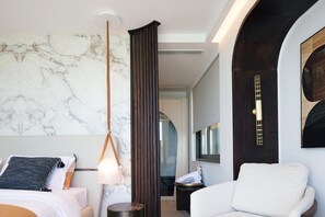 A modern hotel room with a marble wall, a hanging pendant light, a large window, and a seating area with a white armchair. - Naiades Beach Hotel Adults Only (Agios Nikolaos)