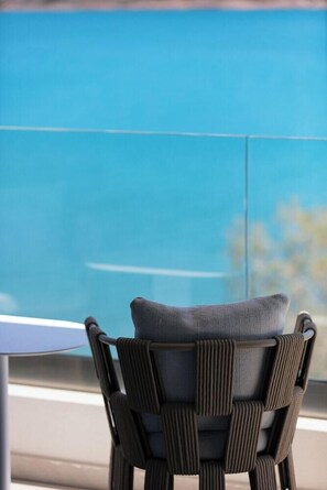 A chair with a woven backrest and a cushion, positioned near a window with a view of the sky. - Naiades Beach Hotel Adults Only (Agios Nikolaos)