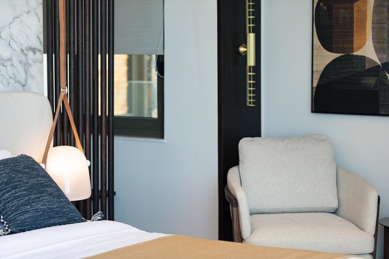 A hotel room with a bed, a chair, a lamp, and a painting on the wall.