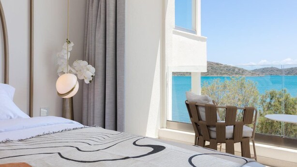 Ein Schlafzimmer mit einem Bett, einem Sessel, einem Tisch und Meerblick.