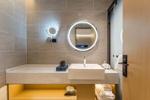 A modern bathroom with a white sink, a round mirror with a light, and a towel rack. - Echarm Hotel (Shanghai)