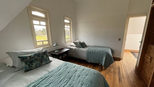 Quarto com duas camas, uma mesa de cabeceira e uma janela.