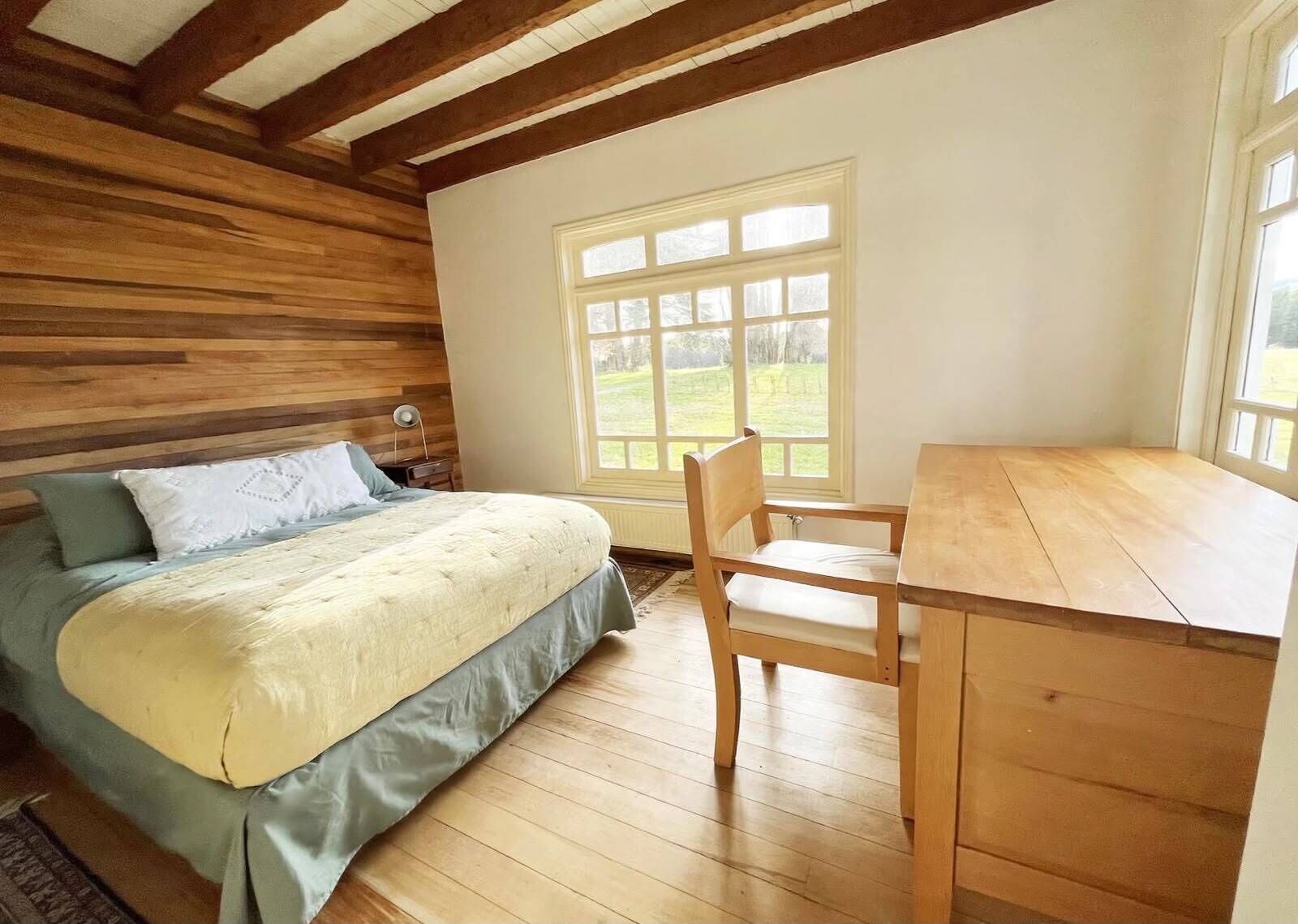 Un dormitorio con una cama, un escritorio de madera y una ventana con vistas a un paisaje verde.