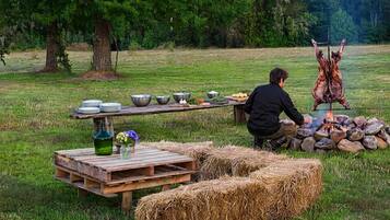 An outdoor dining setup with a wooden table, hay bales, and a fire pit.