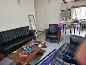 Un salon comprenant un canapé en cuir noir, une table basse en bois avec des appareils électroniques, et un fauteuil en cuir noir.