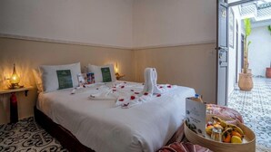 A hotel room with a neatly made bed, a bedside table with a lamp, and a fruit basket on the floor. - Riad Bab el Qamar (Marrakech)
