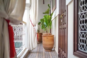A narrow corridor with patterned floor tiles, a potted plant, and a door with intricate metalwork. - Riad Bab el Qamar (Marrakech)