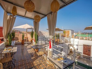 An outdoor terrace with tables and chairs, potted plants, and a view of buildings in the background. - Riad Bab el Qamar (Marrakech)
