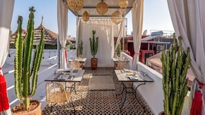 An outdoor terrace with tables and chairs, potted cacti, and a patterned floor. - Riad Bab el Qamar (Marrakech)