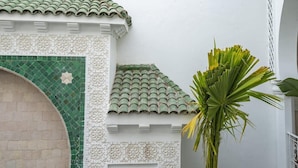 A building with a tiled roof, a decorative archway, and a palm tree. - Riad Bab el Qamar (Marrakech)