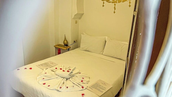 A neatly made bed with a towel arranged in a bow, a bedside table with a lamp, and a wall-mounted light fixture. - Riad Bab el Qamar (Marrakech)