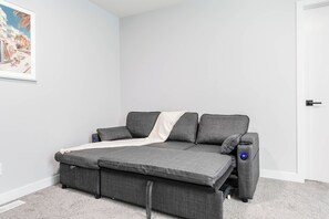 A grey sofa with a white throw blanket and two pillows, positioned against a white wall with a framed picture. - Stylish 3BR Home With A/C | Fast Wifi | Garage Parking | Sleeps 10 (Calgary)