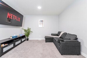 A living room with a sectional sofa, a flat-screen TV mounted on the wall, a small plant, and a framed picture on the wall. - Stylish 3BR Home With A/C | Fast Wifi | Garage Parking | Sleeps 10 (Calgary)