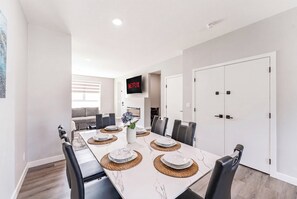 Un espace repas moderne avec une longue table, des chaises et un téléviseur fixé au mur.