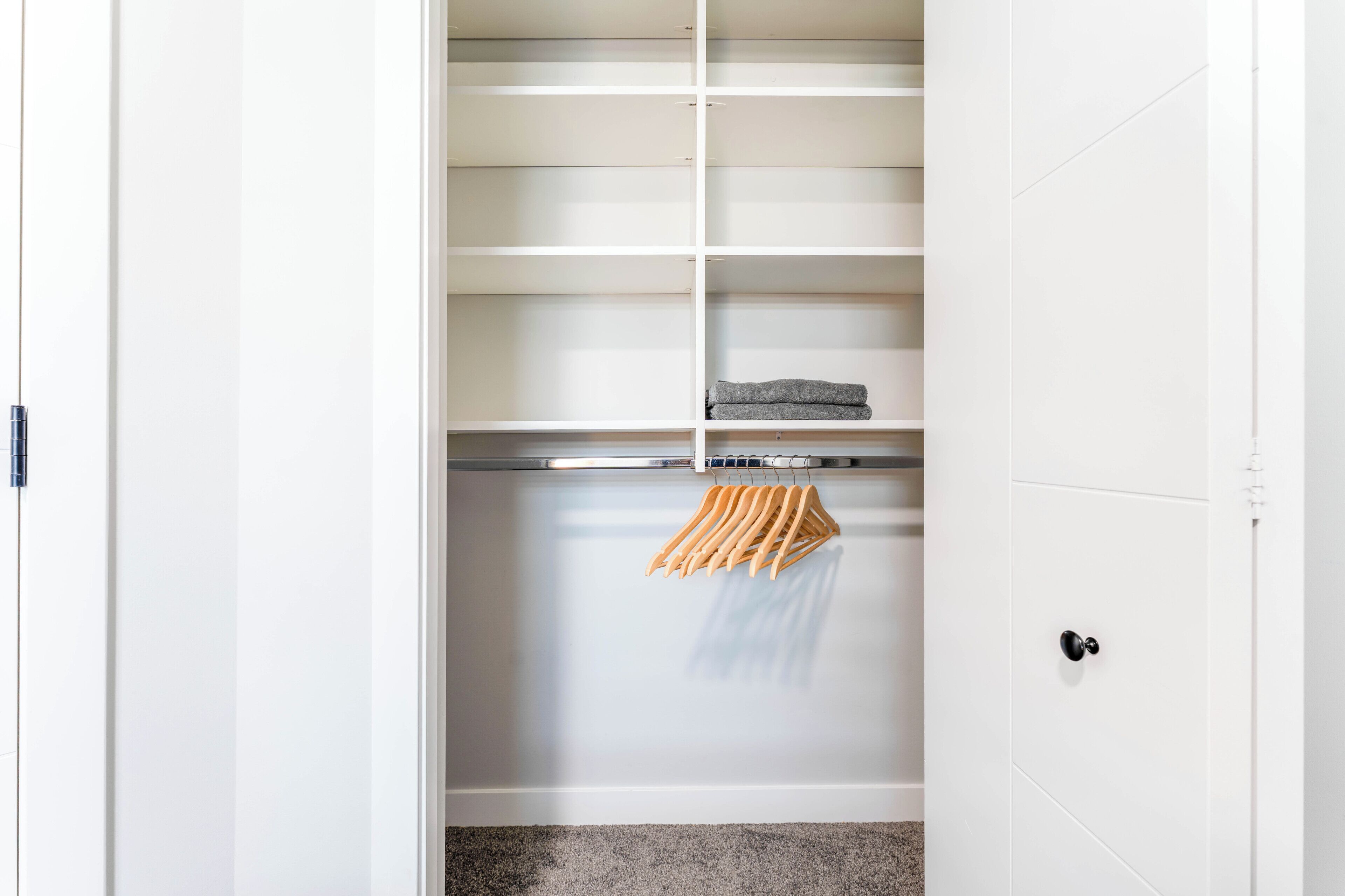 Ein begehbarer Kleiderschrank mit weißen Regalen, einer Metallstange und einem Holzaufhängegestell.