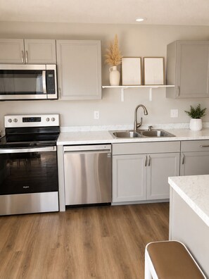 A modern kitchen with stainless steel appliances, a wooden floor, and light-colored cabinetry. - Beautiful and Relaxing Full Townhome 20 Minutes From City (Grandview)