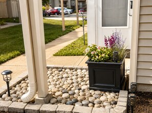A residential entryway with a stone pathway leading to a door, a planter with flowers, and a small outdoor light fixture. - Beautiful and Relaxing Full Townhome 20 Minutes From City (Grandview)