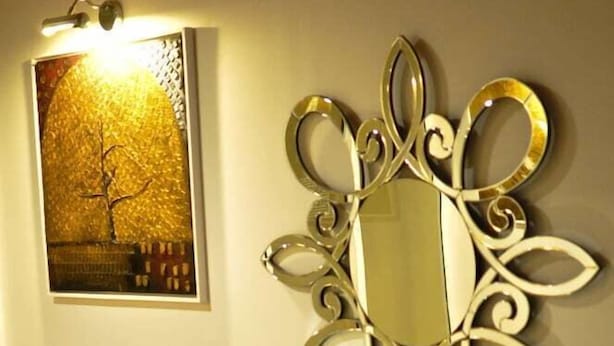 A wall-mounted mirror with an ornate design, a framed picture, and a decorative vase on a console table.
