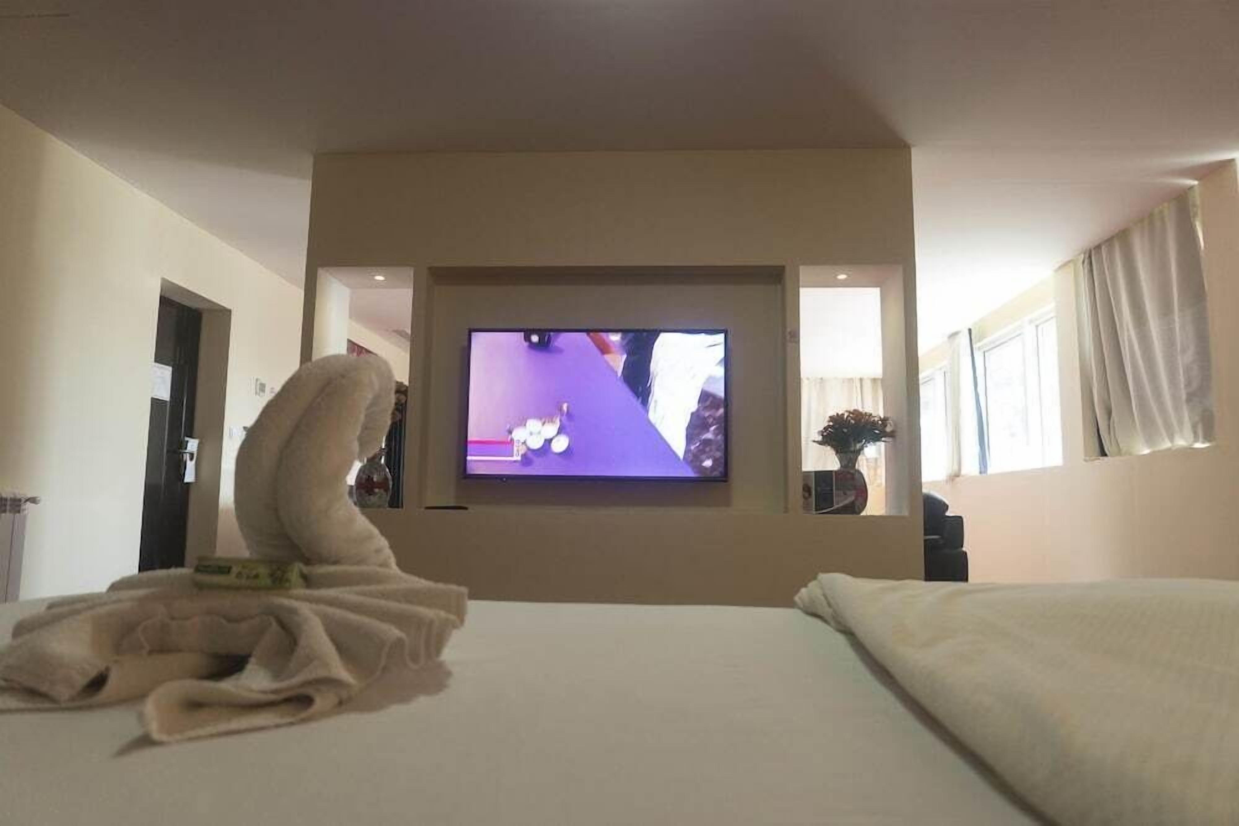 A hotel room with a bed, a television mounted on the wall, and a window with curtains.