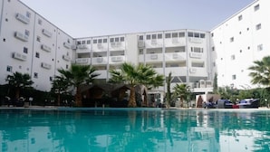 Een hotel met een zwembad, meerdere balkons en palmbomen.