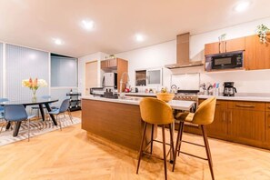 A modern kitchen with wooden cabinets, a central island, and bar stools. - Roma Norte Penthouse, Rooftop & Skyline Views (Mexico City)