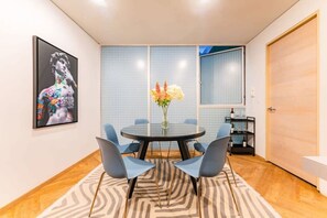 A modern dining area with a round table, four chairs, a vase with flowers, and a wall with a grid pattern. - Roma Norte Penthouse, Rooftop & Skyline Views (Mexico City)