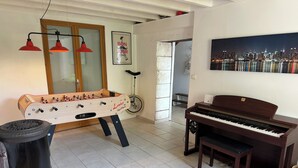 A room with a foosball table, a piano, a bicycle, and a cityscape painting. - Traditional 19th century stone farmhouse sympathetically restored with views. (Saint-Martial-Viveyrol)