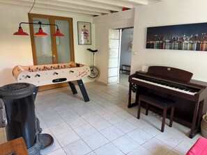 A room with a foosball table, a piano, a bicycle, and a cityscape painting. - Traditional 19th century stone farmhouse sympathetically restored with views. (Saint-Martial-Viveyrol)