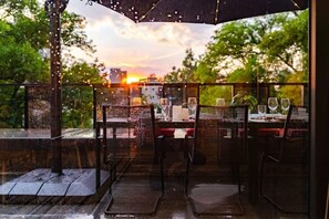 An outdoor dining area with tables and chairs, a view of the sunset, and a glass enclosure. - Polanco Penthouse: Rooftop Swing & City Views (Mexico City)