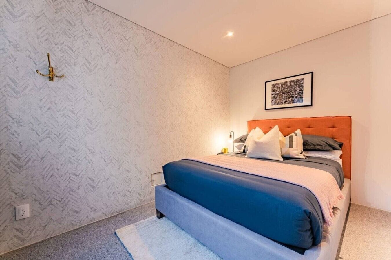 Ein Schlafzimmer mit einem Bett, einem Kopfteil, einer Wandleuchte und einem gerahmten Bild.